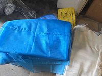 Photo showing folded blue and off-white rectangular polyester tablecloths on a floor.