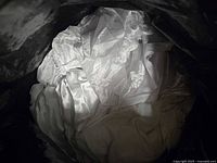 Pile of white fabric seat covers made from satin-like material, shown inside a dark container.