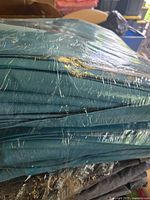 Stack of turquoise polyester table linens wrapped in clear plastic showing folds and color.