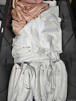 Top-down view showing a textured pink tablecloth and several white cloth pieces, folded and stacked in black drawer or container.