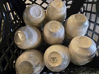 Top-down view of multiple teacups arranged upside down in a black basket, all wrapped in clear plastic film.