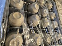 Photo of 12 ivory teacups upside down arranged in cardboard box, each wrapped in plastic for protection.