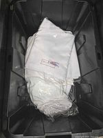 White new linens tightly folded and wrapped in plastic in a black plastic container.