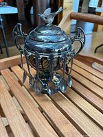 Close-up shot of antique silver-plated sugar bowl with decorative bird lid and hanging teaspoons.