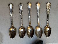 Five teaspoons aligned horizontally on gray surface