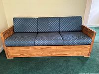 Front view of a blue fabric upholstered sofa bed with a wood frame and three seat and back cushions