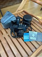 Photo showing Canon T50 camera body with 50mm lens attached, camera strap, both lens cases, and two manuals on a wooden surface.