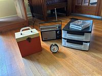 Full lot showing vintage Sony radio, analog clock, vinyl storage box, CDs stacked on plastic drawers, and plastic 3-drawer storage unit.