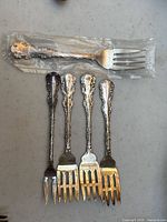 Five forks arranged flat—one in plastic bag at top, four identical slotted forks below