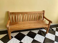 Front view of teak bench against a yellow wall showing slatted seat and back