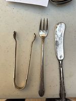 Top view of three sterling silver serving utensils: tongs, serving fork, and butter spreader showing pattern details and wear