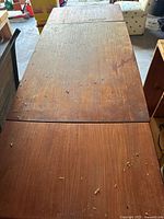 Top view of large wooden table with visible scratches, marks, and debris on surface showing medium to dark brown finish.