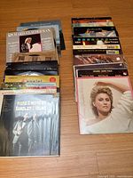 Top-down view of two stacks of vinyl albums arranged vertically on a wooden floor showing album covers such as Richard Clayderman and ABBA.