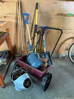 Photo showing the full lot with various garden and yard tools including metal shovels, a red plastic garden cart, watering can, and a metal pail with soil.