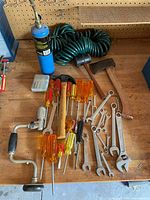 Overview of entire tool lot showing mixed hand tools including screwdrivers, wrenches, hammers, soldering torch, coil hose, hacksaw and box of bits