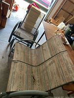 Photo of outdoor patio glider bench showing green metal frame, beige/tan mesh fabric seat and back with geometric pattern, seating 2 people.