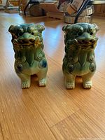 Front view of pair of green ceramic Foo Dog statues with blue highlights showing detailed facial features and surface texture.