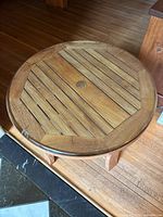 Full view of the round wooden table top showing the slatted wood design with a framed rim, minor wear and scratches visible.