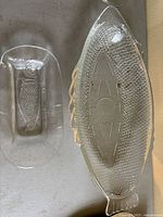 Overhead view of the two clear glass fish-shaped platters, showing embossed scale details and shape