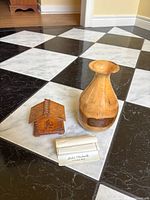 Both the wooden vase and the trinket box set displayed on a black and white tiled floor with a leaflet included.