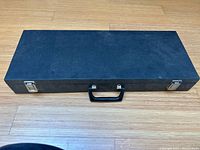 Closed black carrying case with metal latches and handle, showing the exterior protective container that holds the miniatures.