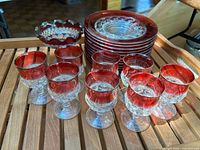 Photo showing 8 goblets, 1 bowl and 4 plates arranged on a wooden surface. Clear glass with ruby red flash band around rims visible with textured patterns.