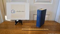 Blue hardcover book standing upright showing titles on spine, placed on wooden surface next to a ruler for scale.