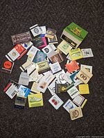 Match books scattered on a dark carpet, showing a variety of vintage brand logos and styles.