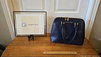 Full view of navy blue Adrienne Vittadini purse with handles on wooden surface and ruler for scale.