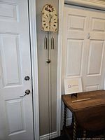 Photo showing full antique German pendulum wall clock mounted on wall with wooden face painted with floral details and Roman numeral dial, two metal weights, and brass pendulum.
