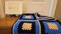 Blue granny square crochet throw folded and displayed on a wooden surface in front of a white door.