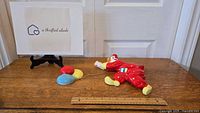 Chalkware clown and balloons laid on a wooden surface next to a ruler for size reference.
