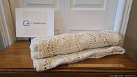 Folded cream coloured crochet blanket on wooden surface, showing texture and scale with ruler nearby.