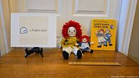 Raggedy Ann dolls and children's book arranged side by side with ruler for size reference.
