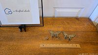 Two solid brass butterfly wall hooks laid on a wood surface next to a ruler and original brass screws, showing size and condition.