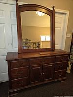 Front view of dark wood 7 drawer dresser with attached arched beveled mirror showing drawer and cabinet details.