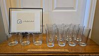 Group photo showing twelve tall and three short clear Libbey Crisa glass tumblers arranged on a table with a ruler for scale.