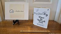 Photo showing Where the Sidewalk Ends book with dust jacket standing vertically on a wooden table, a ruler in front for scale, and a small framed sign 'a thrifted abode' next to it.