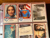Close-up photo of 9-pocket sleeve containing six trading cards including character portraits and scenes from the 1978 Superman movie.