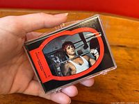 Front view of top sticker featuring Sylvester Stallone as Rocky in a white tank top, held in a hand showing the protective case.