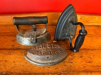 Pair of antique sad irons and detached component on wooden surface with red background