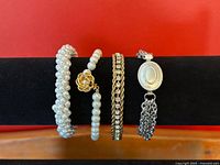 Four vintage bracelets arranged side by side on black display stand showing details of each design and clasp