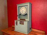 Full view of tall antique employee punch clock with painted wooden case in mint green, round clock face, and base with crank lever and time card slot.