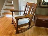 Three-quarter front view showing oak frame, wide arms, grey cushion and rocker rails