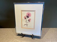 Framed and matted botanical art print featuring pink thistle on display stand against neutral background