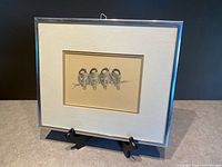 Framed print on display showing four chickadees perched closely on a branch in soft detail, double-matted and framed in chrome metal.