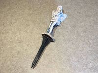 Garden fairy figurine with ground stake laid on concrete floor, showing the entire figurine and stake from a top perspective.