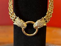 Close-up of gold-tone panther heads gripping central ring showing rhinestone eyes and texturing.