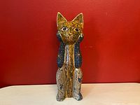 Front view of tall hand-carved wooden cat sculpture painted in golden yellow, navy blue, and black with folk art-style celestial motifs.