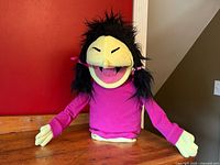 View of full half-body handmade puppet with black hair in pigtails, pink shirt, and animated facial features.